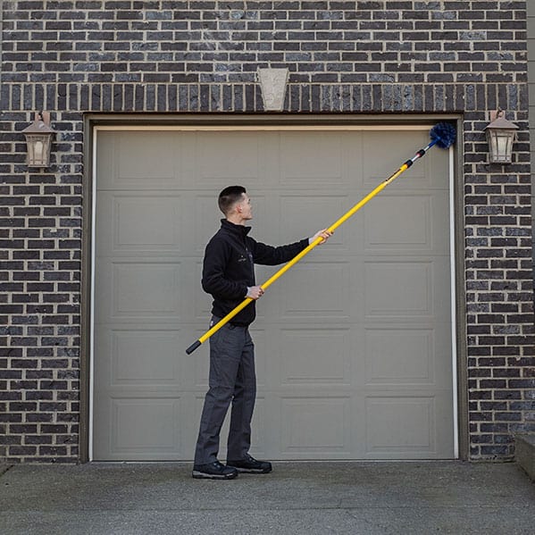 Aspen Pest Control technician cleaning the corners of a garage door for webs