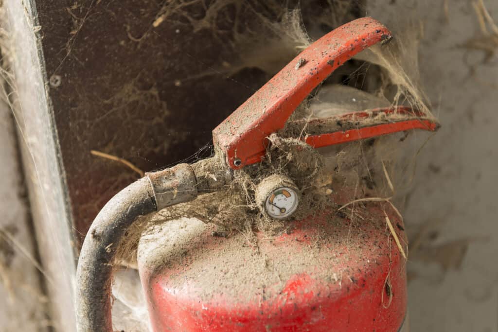 Dirty fire extinguisher that is covered in spider and cobwebs